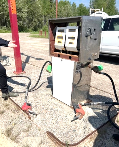 A defunct gas pump, with broken glass at the base and the pump handles laying on the ground.