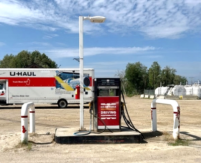 Un poste d'essence qui n'est plus en service. Des réservoirs de carburant sont visibles à l’arrière-plan, près de la limite forestière de la propriété.