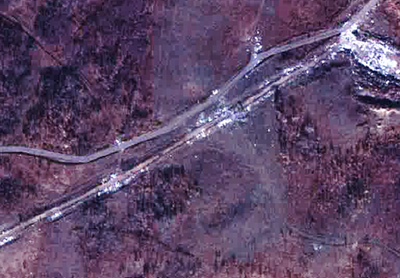 A satellite image showing a road with visible piles of waste at regular intervals.
