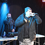 A rapper performing on stage while a DJ plays in the background.