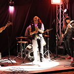 A metal singer, joined by his band, performing under the outdoor tent. 