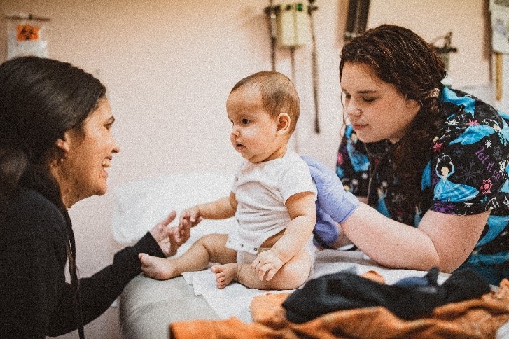 Une infirmière examine un bébé pendant que la mère garde son attention.